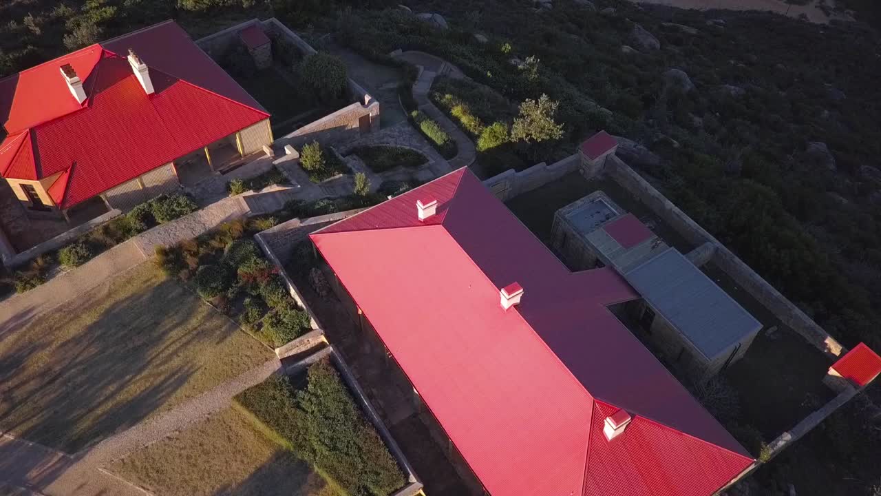 toma aérea de propiedades de techo rojo en la colina con dos playas y vista al mar junto a un faro