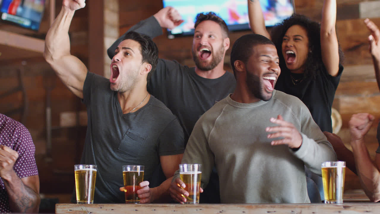 grupo de amigos masculinos y femeninos celebrando mientras ven el juego en la pantalla en un bar deportivo