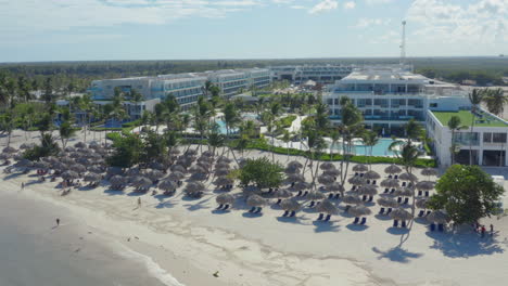 Palm-trees-and-straw-parasols-on-beach-of-luxurious-hotel-resort