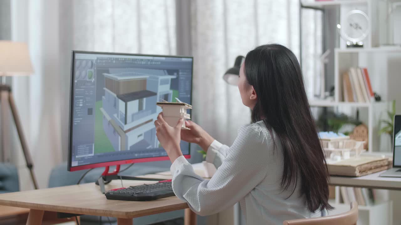 Asian Woman Engineer Holding And Looking At The Small House Model With Solar Panel While Designing House On A Desktop At Home. Cyber Games House Design And Decoration