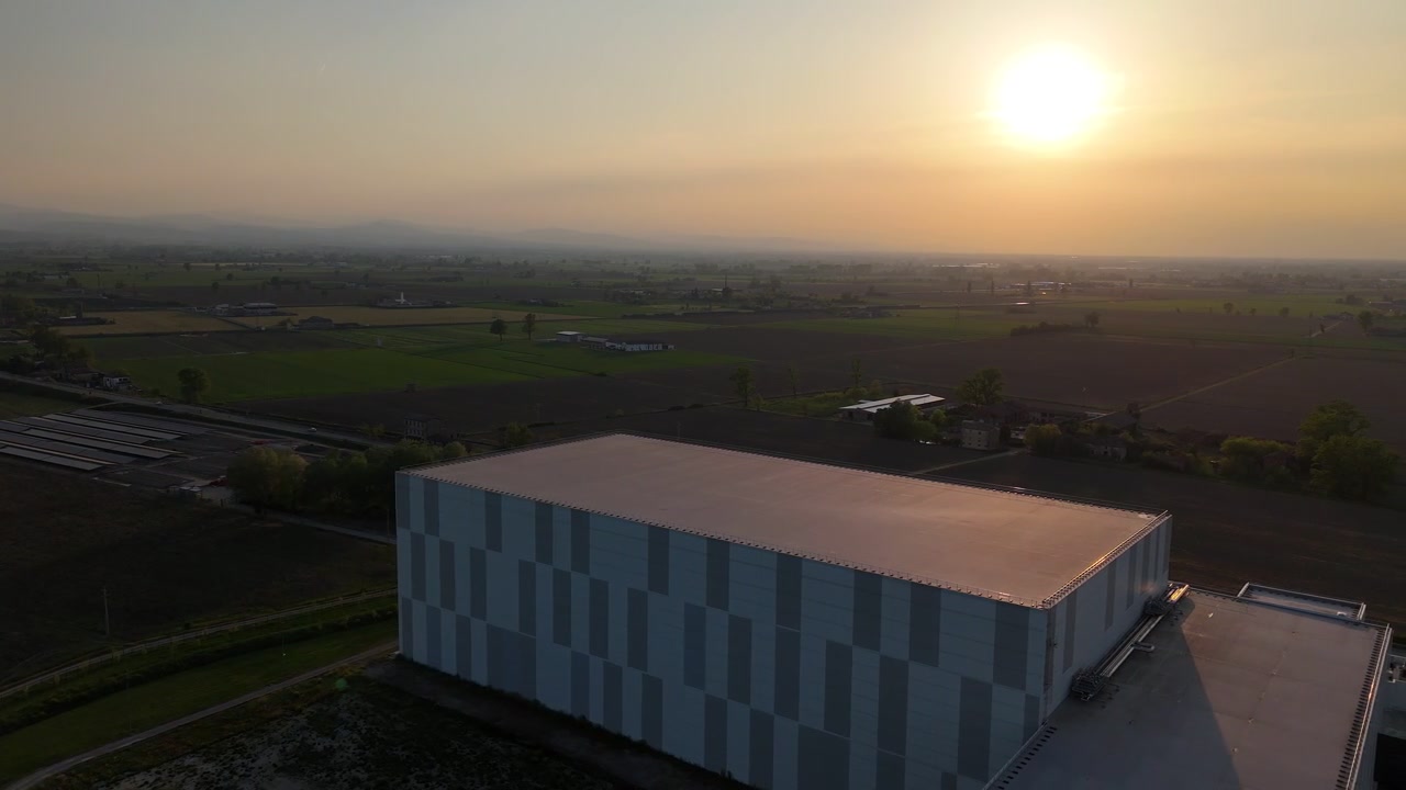 Automatiseret kølelager nær Fiorenzuola d'Arda, Piacenza, Emilia Romagna, Italien, med et stort kølelager og logistikoperationer, beliggende i landbrugsområdet Pianura Padana under solnedgangens skær.