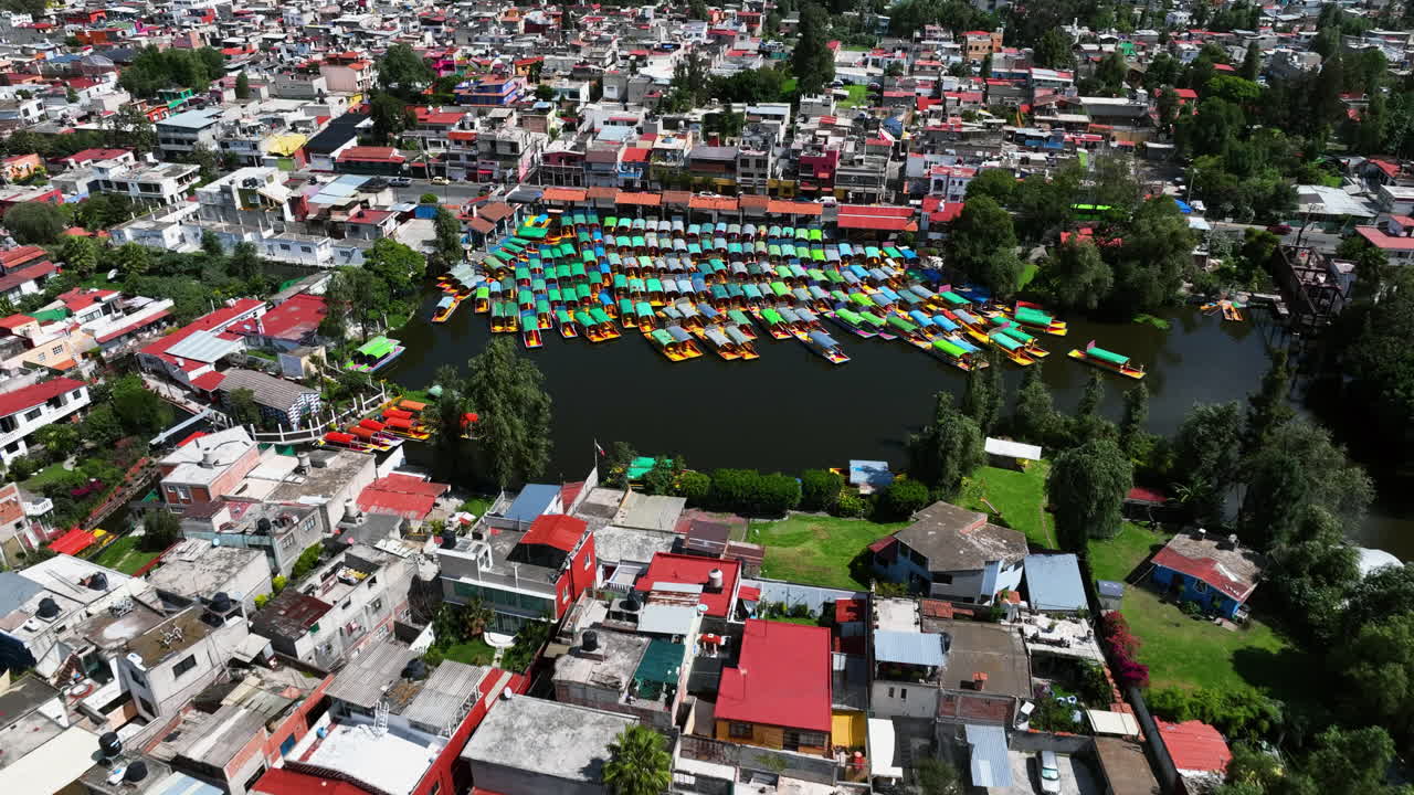 drone se acerca a un muelle con barcos trajinera atracados en xochimilco, ciudad de méxico