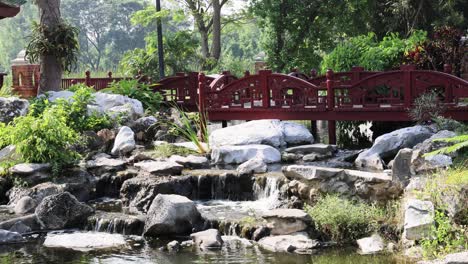 tranquil garden scene with flowing water and red bridge