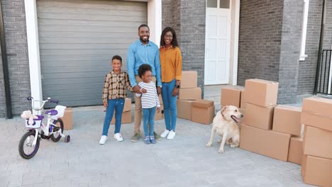 retrato de una familia afroamericana feliz con niños pequeños y un perro parado en una casa nueva en el suburbio