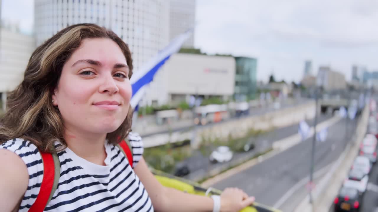A woman is waving at the camera in front of a tall building
