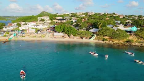 drone pullback reveals white sandy beach of boca sami with fishing boats anchored in clear water