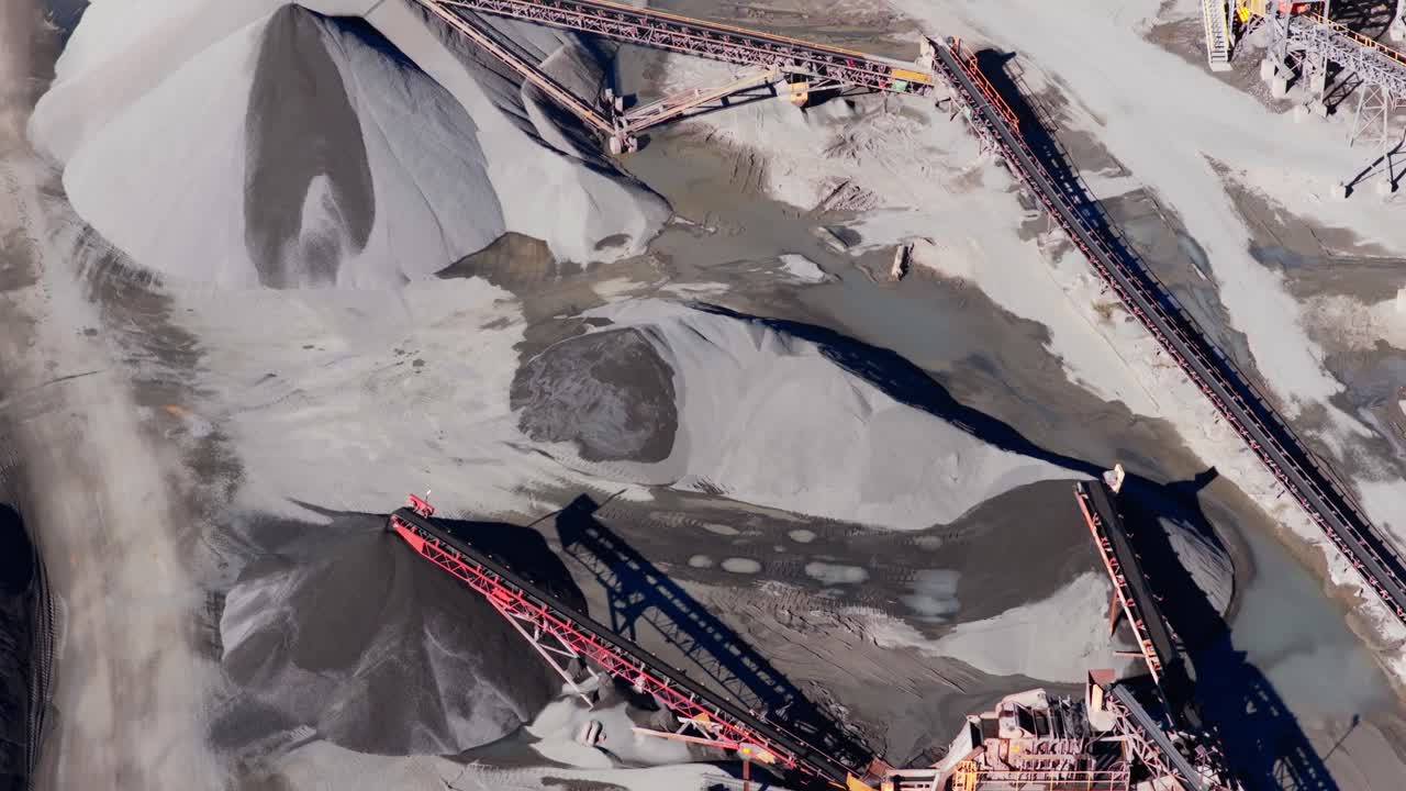 Aerial pullback along quarry conveyor system and gravel piles, moving crushed stone across aggregate processing plant