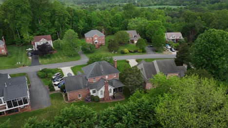real estate houses in brick design between green forest trees. drone approaching. cloudy day in spring. parking garages in quiet noble housing area.