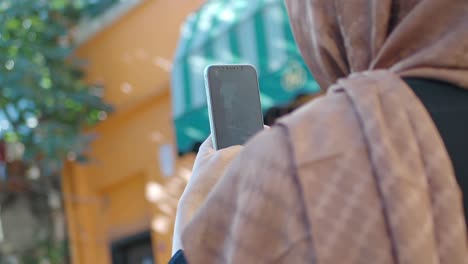 mujer en hijab tomando una foto con su teléfono celular en la calle