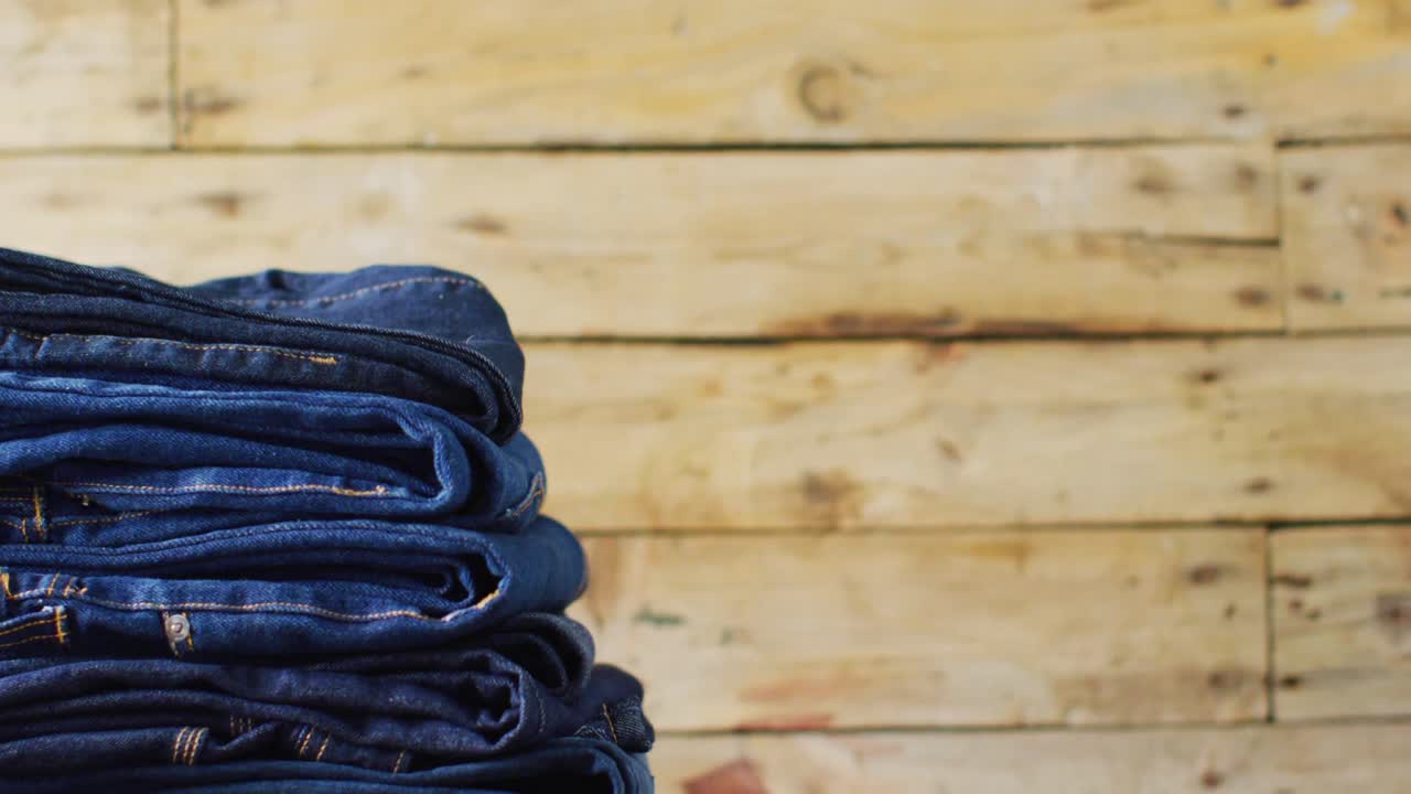 Close up of folded jeans with different shades on wooden background with copy space