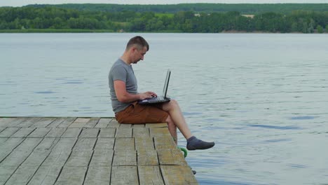 young man working on laptop while sitting ?n old pier