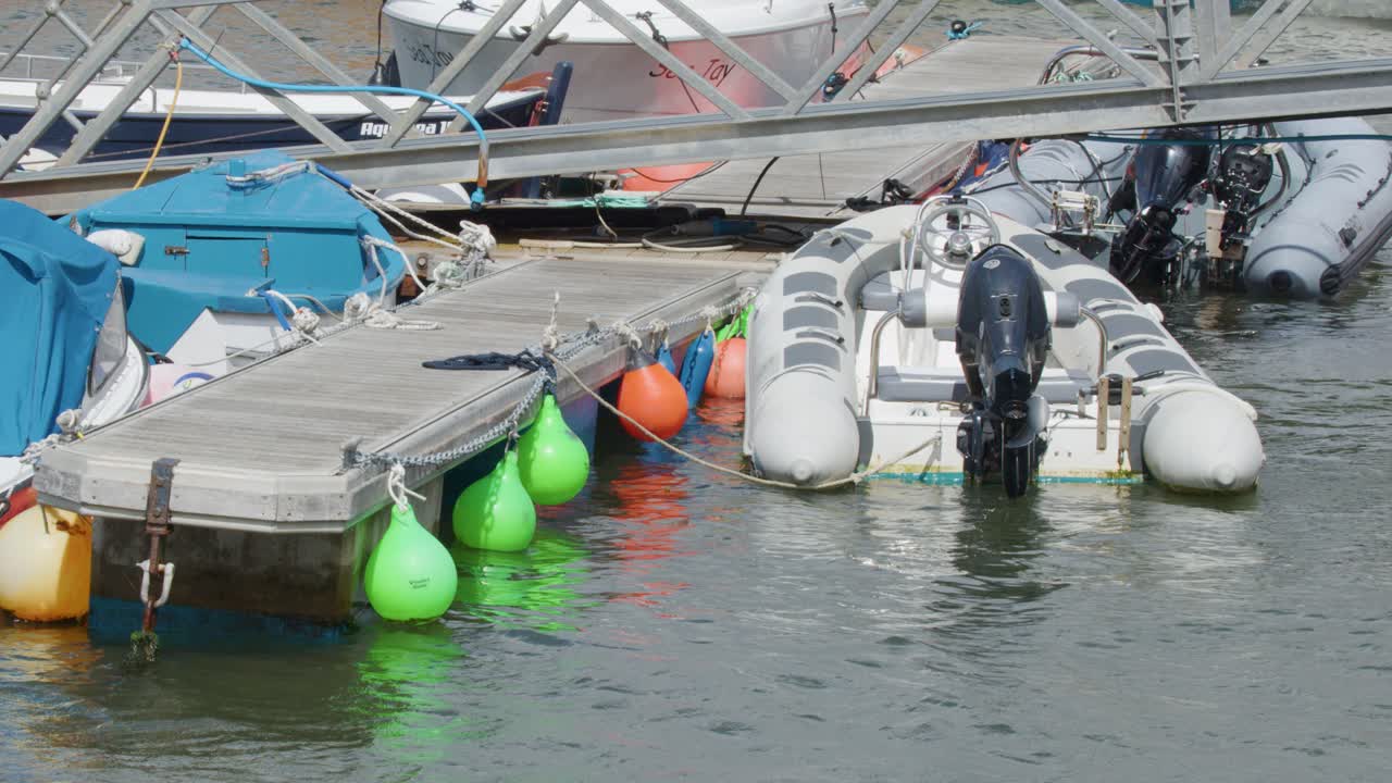 Rigid inflatable boat approaches floating dock with colorful buoys in busy Cromarty, Scotland marina