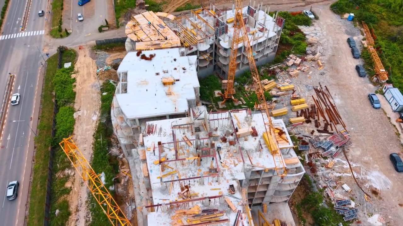 Vista aerea del braccio di una gru a torre gialla su un cantiere edile. Vista dall'alto di un braccio di gru giallo sopra il solaio in cemento di un edificio non completato, accanto a un'autostrada asfaltata.