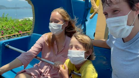 slowmotion shot. a family wearing protective face masks is riding on a giant swing. selfie video. visiting parks among pandemics