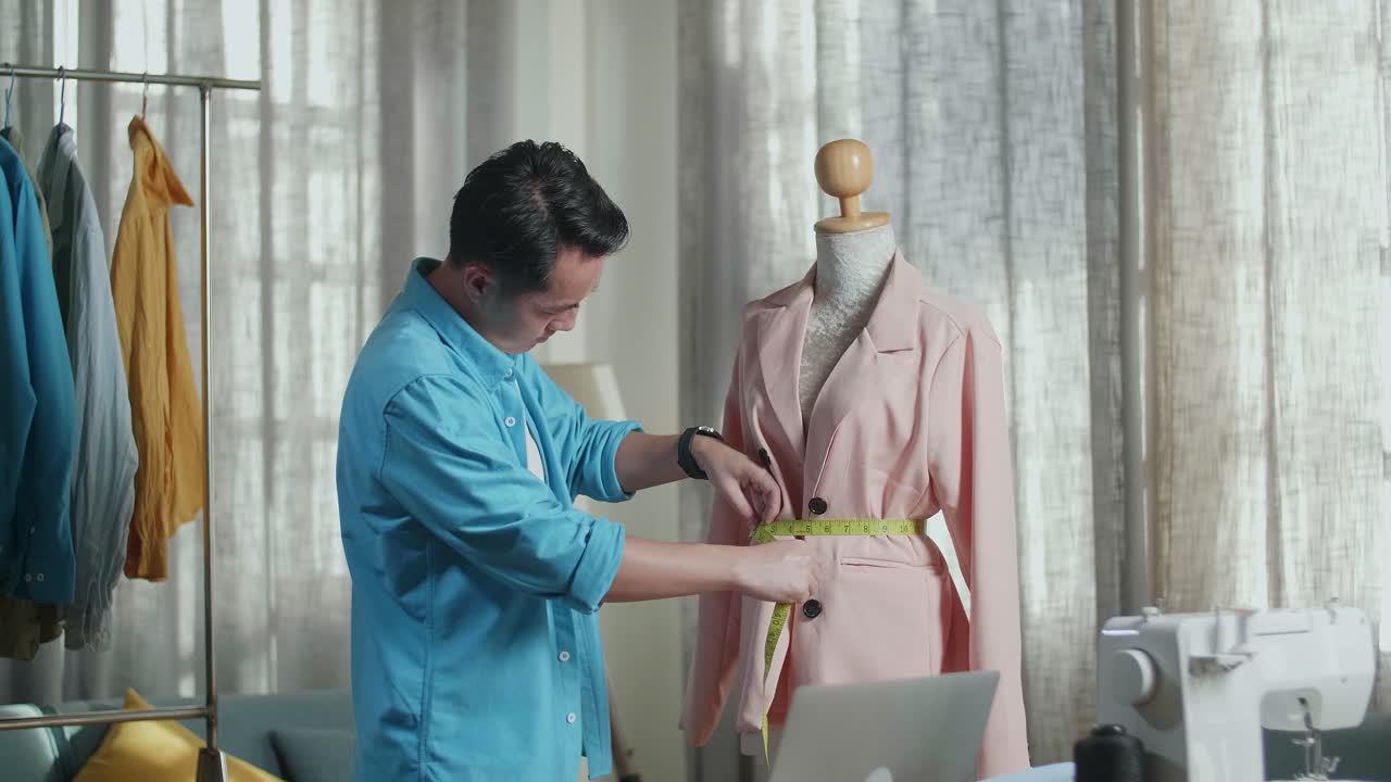 アジアの男性デザイナーがスタジオで服をデザインしている間マネキンでジャケットを測定する縫製機を持っています