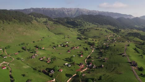 Un-Pintoresco-Pueblo-Ubicado-En-Colinas-Verdes-Con-Fondo-Montañoso,-Bajo-Un-Cielo-Despejado,-Vista-Aérea