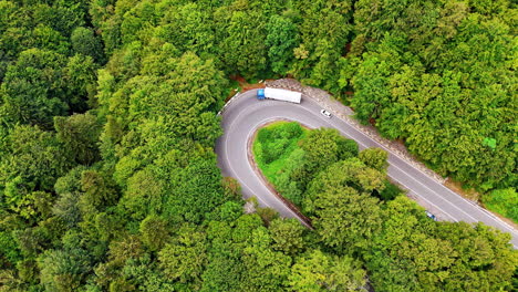Curvy road in green forest. A truck and a car navigate a curvy road surrounded by dense trees in a vibrant green forest during the day