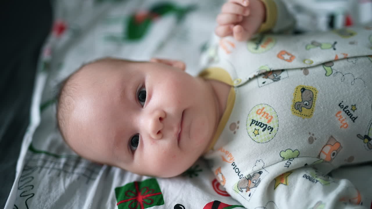 Healthy active Caucasian baby boy lies on his back. Sweet adorable child looks at camera and waves his hands and legs. Close up.