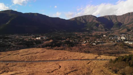 Slow-aerial-sideways-flight-over-beautiful-yellow-grassland-with-green-mountains-and-car-traffic