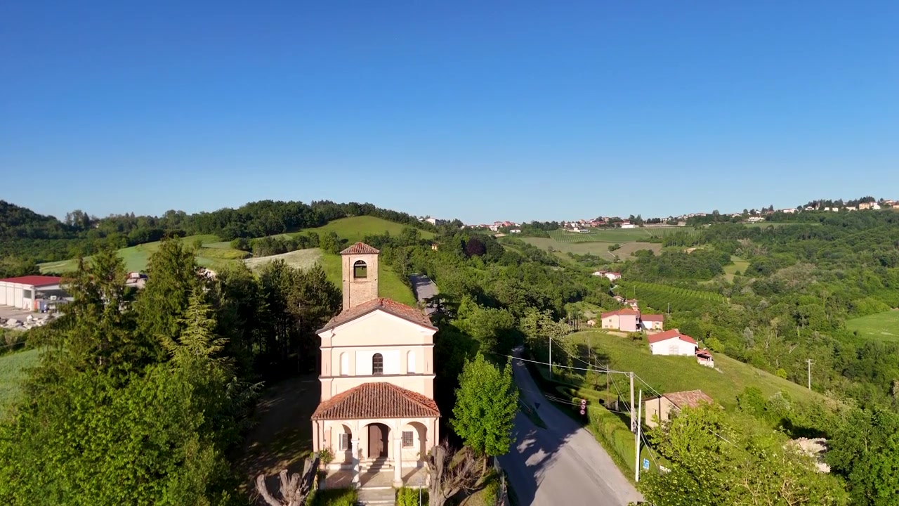 Un filmato di drone si eleva sopra una cappella rurale, rivelando rigogliose colline verdi e l'architettura della campagna europea.