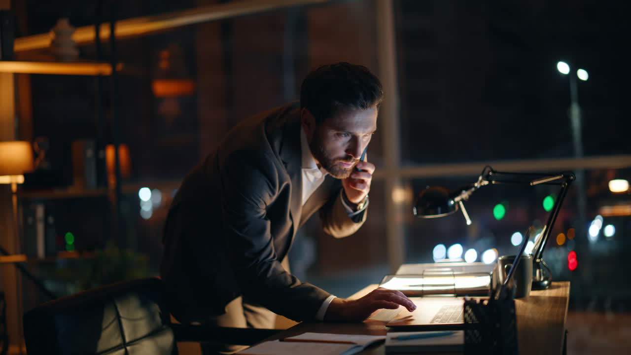 Bearded leader talking cellphone standing office window looking night city view