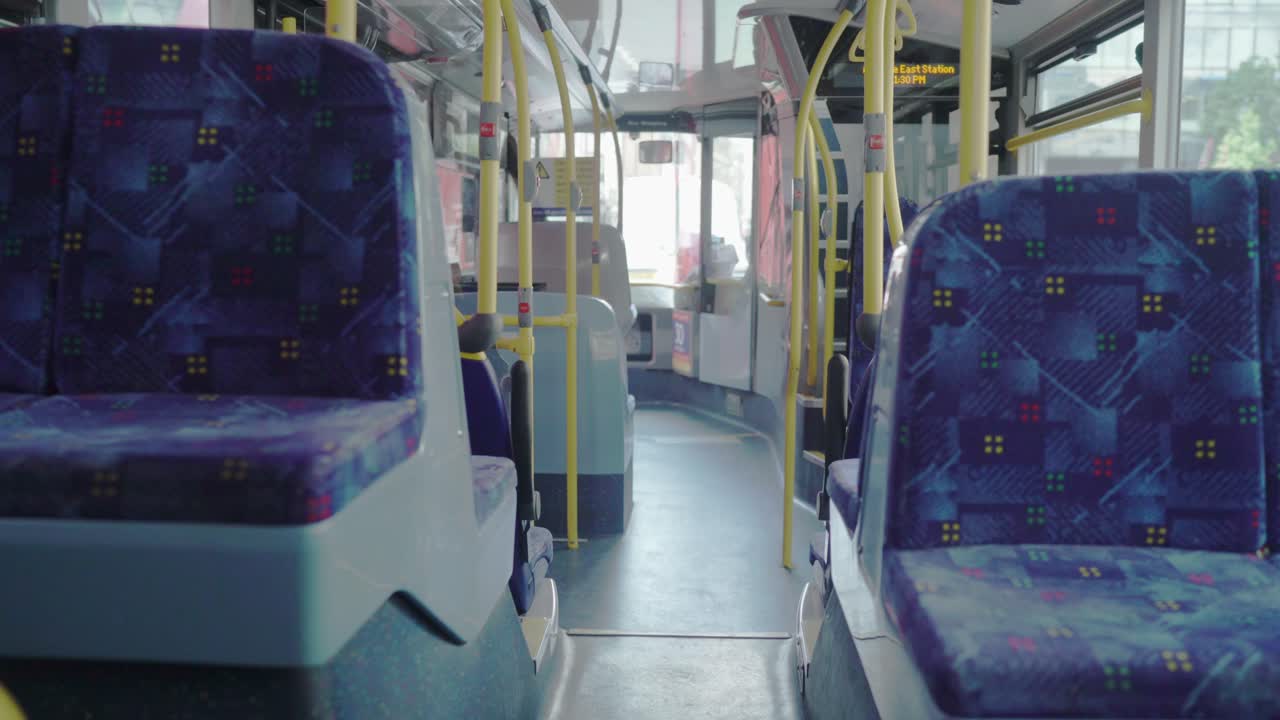 An empty bus in London with blue seats while driving in the traffic as other red buses and cars passing by