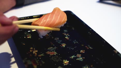 last piece of sake nigiri sushi is plucked from plate with chopsticks