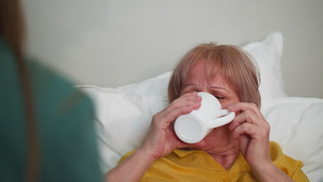 unquiet senior woman drinks pills looking at nurse