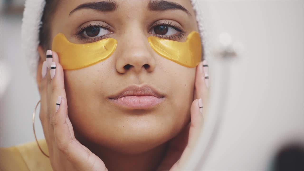A closeup portrait of a beautiful woman after a bath with a towel on the head puts patches under the eyes from wrinkles and dark circles.