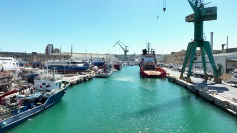 Aerial-drone-shot-flying-low-over-blue-sea-in-between-several-boats-and-ships-in-a-very-busy-boat-yard