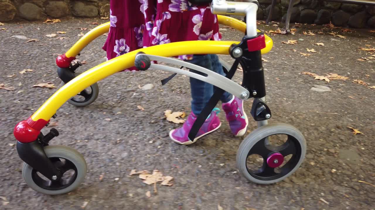 niña negra con parálisis cerebral caminando en el parque con su dispositivo de asistencia