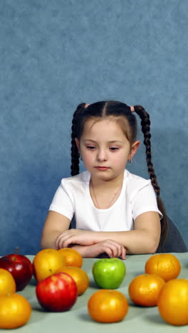 cheerful kid with fresh fruits. little girl sitting at the table full of ripe organic fruits. healthy food concept. vertical video