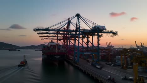 dramatic sunset over busy port: cargo ship loading with cranes in operation, showcasing logistics and maritime activity in a vibrant harbor environment