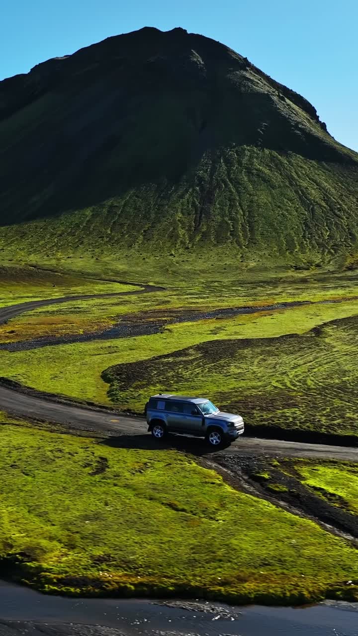 Drone aereo di un SUV 4x4 che guada un fiume poco profondo su una strada sterrata remota in una valle verde di montagna, epica avventura estiva via terra
