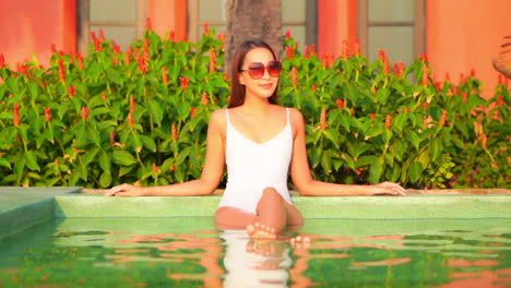 Vista-Frontal-De-Una-Mujer-Asiática-En-Una-Piscina-Con-Traje-De-Baño-Blanco-Y-Gafas-De-Sol