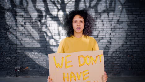 Serious-young-environmental-protester-holding-a-cardboard-with-We-don't-have-time"-inscription-and-protesting-while-looking-at-the-camera"