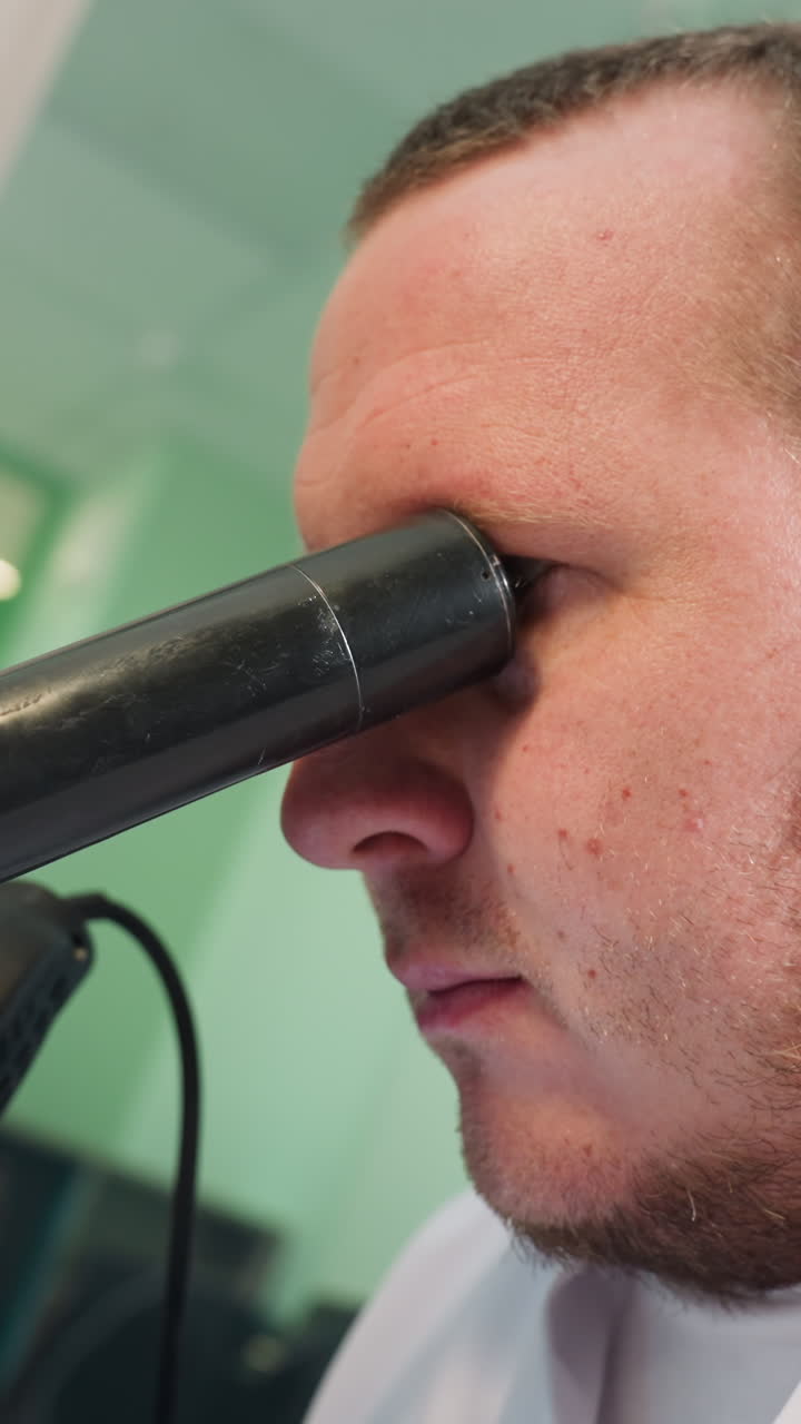 una vista de cerca de un técnico enfocado usando un microscopio para examinar detalles intrincados, el técnico lleva una bata de laboratorio