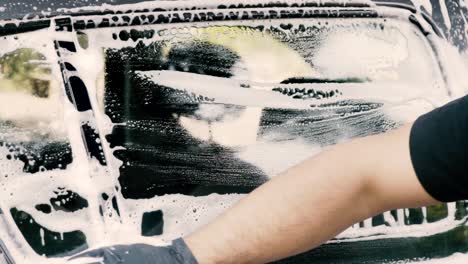 Close-up-of-a-male-washing-a-car-wearing-a-black-gloves-with-shampoo-and-sponge