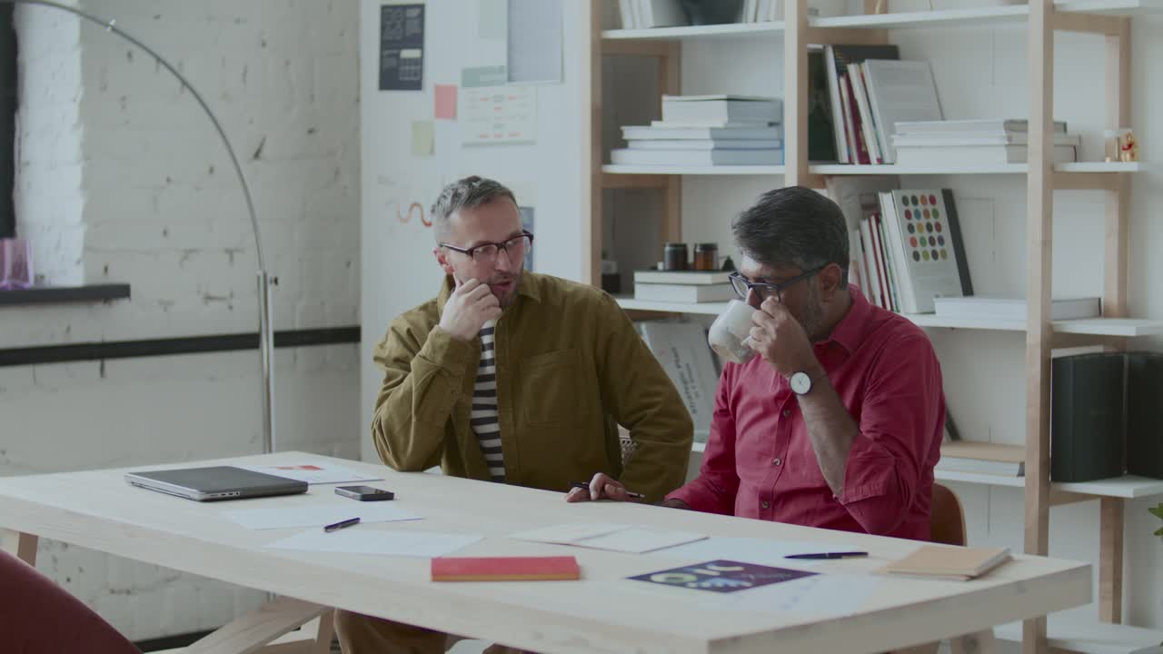 Two Male Colleagues Discussing Work at Table in Minimalist Office