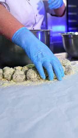 confectionery worker covers the biscuits with sprinkling. female hands take the sweets, puts them into a metal bowl, mixes and puts them on a tray. vertical video