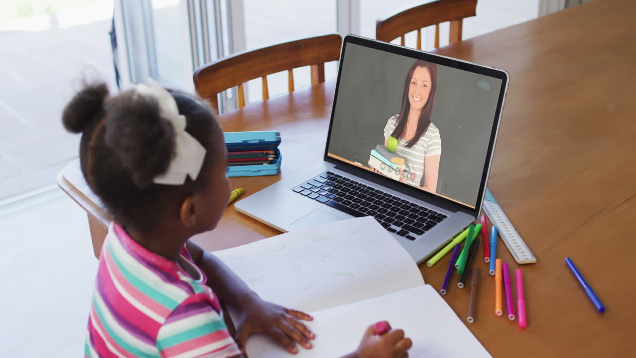 African american girl doing homework while having a video call with female teacher on laptop at home