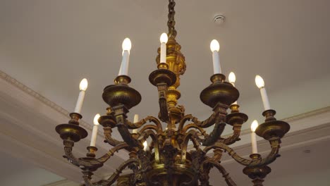 Close-gimbal-shot-of-gilded-bronze-electric-chandelier-against-the-ceiling-of-the-king-style-castle