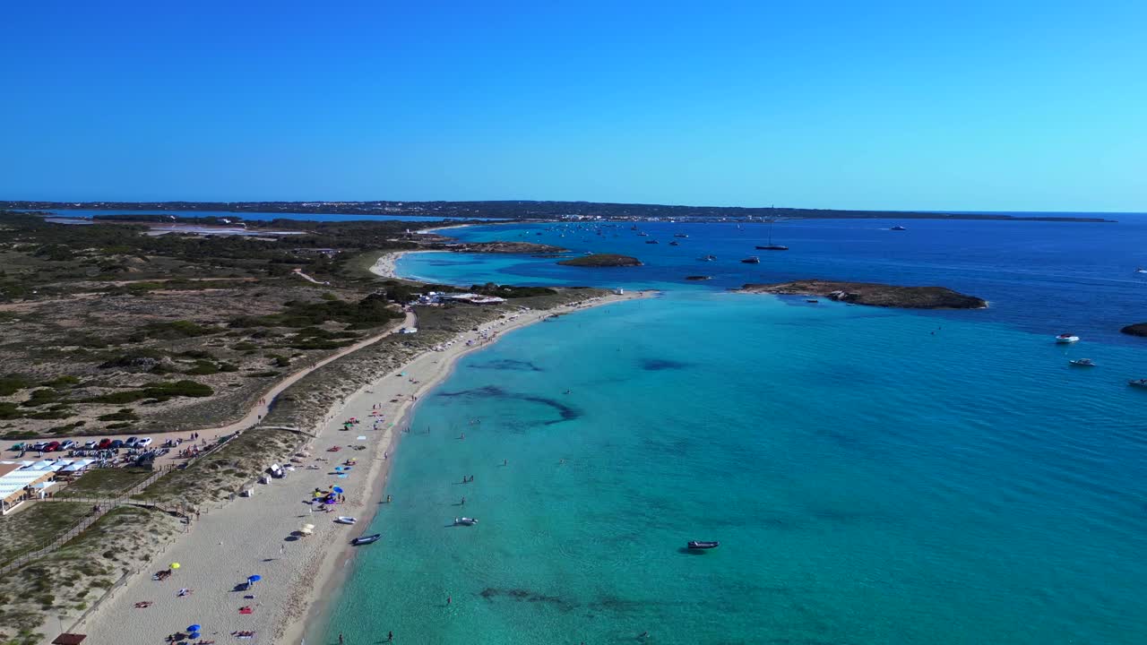 Spiaggia di Platja de Ses Illetes a Formentera con oceano turchese cristallino e persone che si rilassano sotto un cielo limpido. Vista aerea unica, sorvolo, drone che avanza