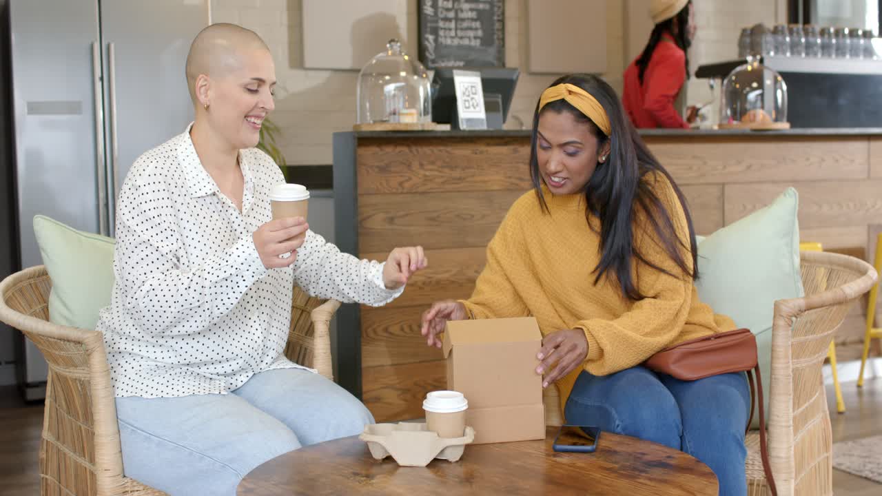 Diverse female friends lifting takeout box lid at coffee shop, revealing cupcakes and catching up