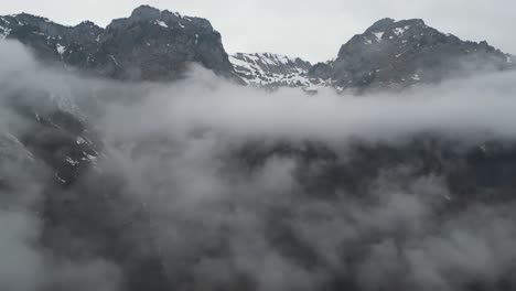 안개 인 구름이 낮게 매달려 있으며, 알파인 산맥의 서사시적인 산맥의 바위와 눈이 하늘로 어 나옵니다.