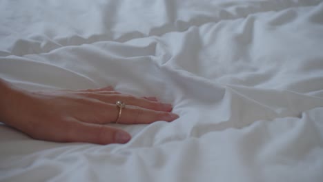 Sensual-female-hand-curiously-feeling-white-sheets-of-empty-bed,-closeup