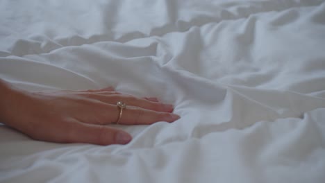 sensual female hand curiously feeling white sheets of empty bed, closeup