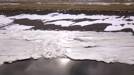 Drone-shot-of-edge-of-land-with-snow-and-ice-forming-near-Selfoss-Iceland