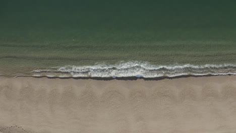 A-top-down-shot-of-small-waves-lapping-a-golden-sandy-beach