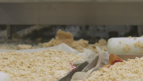 close up of hands of workers rolling and preparing crumble mix on top of a large scale production baking tray